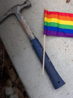 Photo of a hammer and pride flag laying on the cement together.