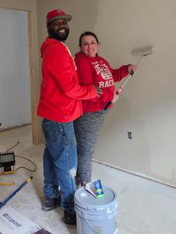 A couple is painting the walls of an unfinished room together.