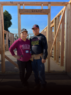 A woman and a man pose together on a construction site for a future Habitat house. 