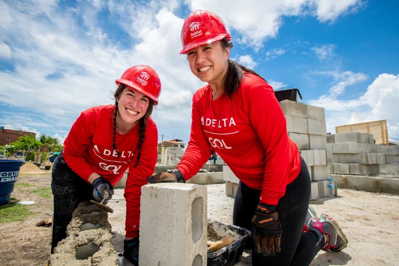 Two women smiling and laying bricks.