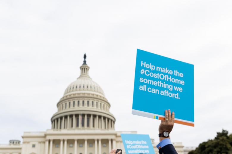 U.S. Capitol building with hands holding up posters about affordable housing.