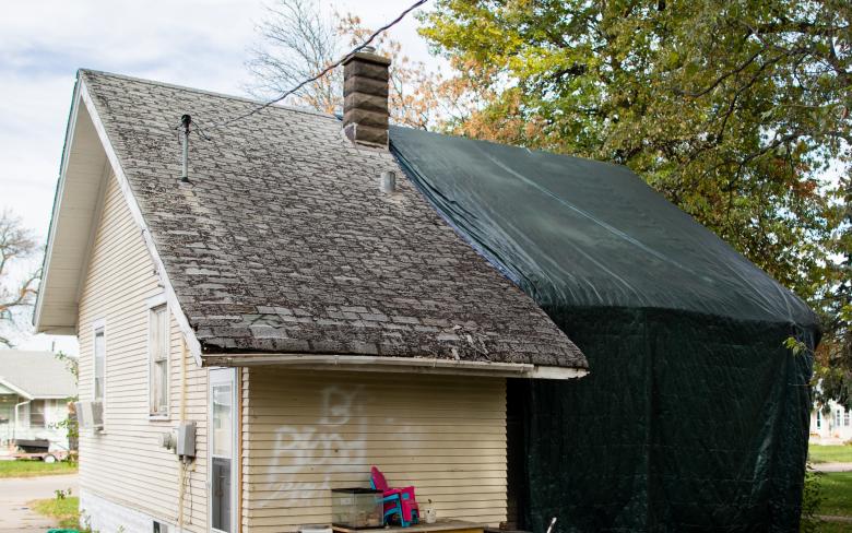 One-story house with tarp over half of it and graffiti 