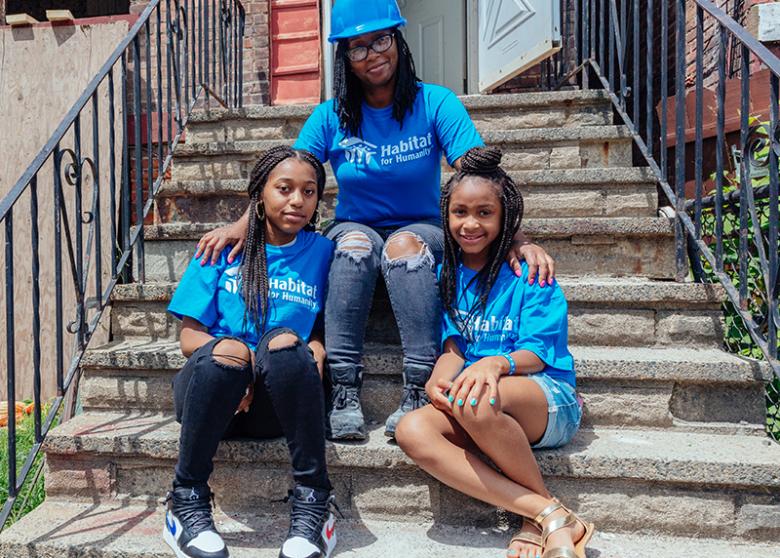 Mom and her two girls sitting on stoop of home with lumber used from Rockefeller tree.