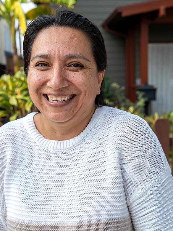 Woman in white sweater smiling with her home in the background.