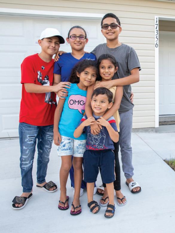 Family of six hugging in front of their home.