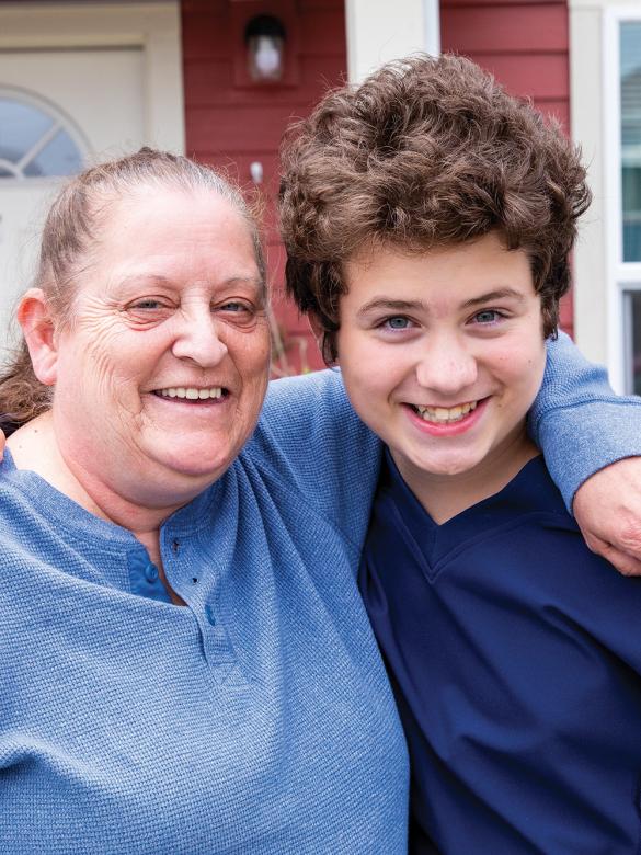 Grandmother and grandson smiling together in front of their home.