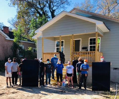 A group of volunteers in front of a partially built blue house.