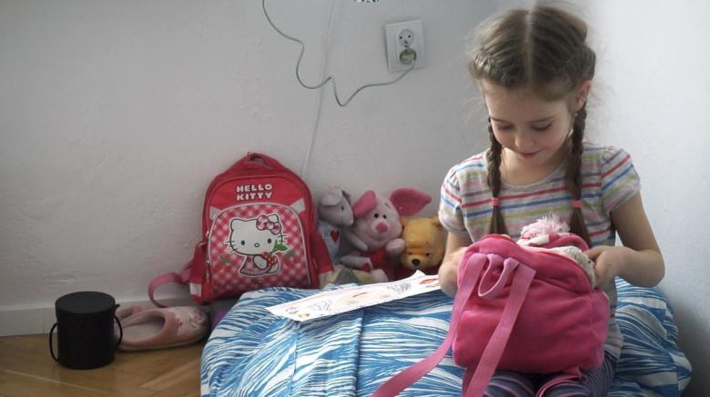 Little girl sitting on a bed looking into a backpack.