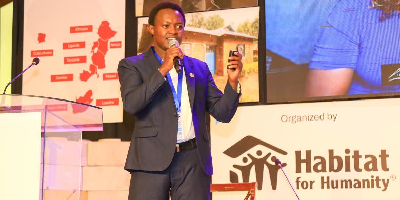 Man in suit presenting on stage with Habitat banner behind him.