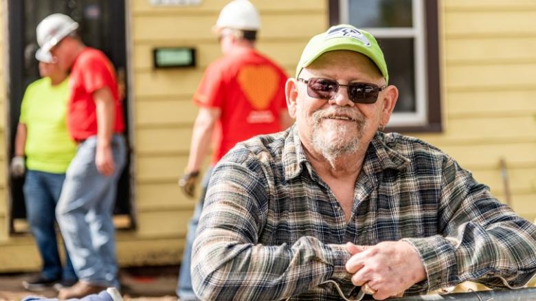 Robert smiles in front of his home with Habitat construction volunteers visible in background.