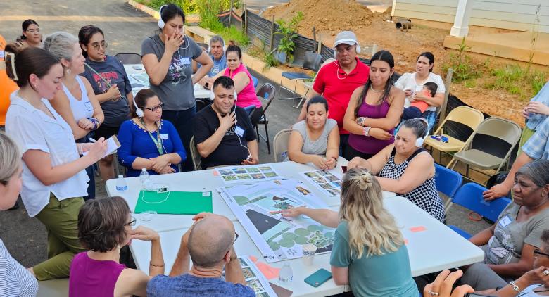 A group of residents gather around a table outside to discuss neighborhood plans.