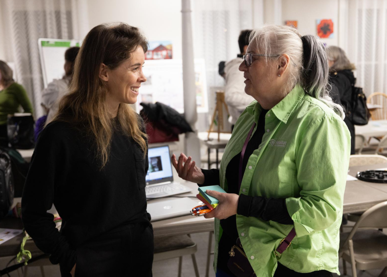 Woman on left smiling and listening as woman on right speaks to her.