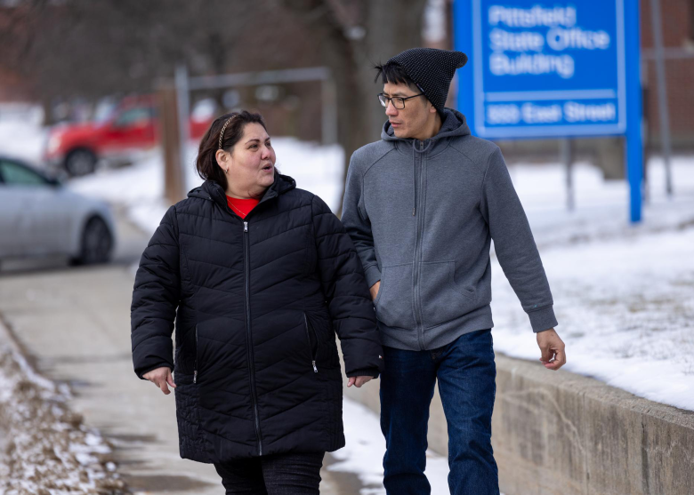 Woman on left speaking to man as they walk towards the DMV building.