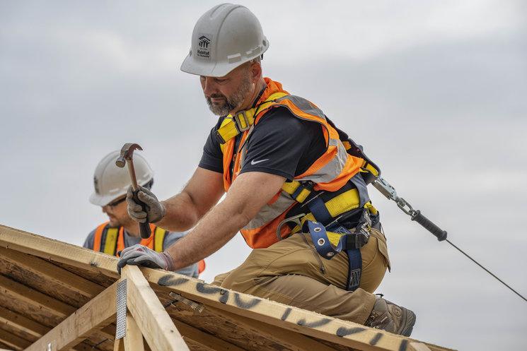 Brandon, wearing construction gear and hard hat, hammers on a roof